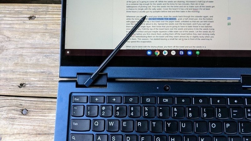 Lenovo ThinkPad C13 Yoga Chromebook tumbado sobre una mesa de madera con un lápiz en la parte superior de la pantalla.